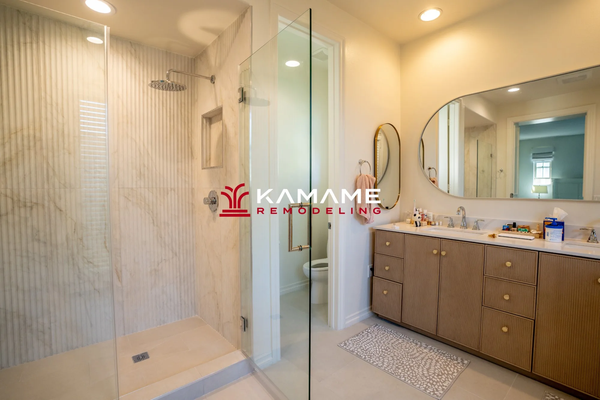 Bathroom remodel with a fluted stone-look shower wall, a frameless glass door, and a double vanity with fluted cabinets